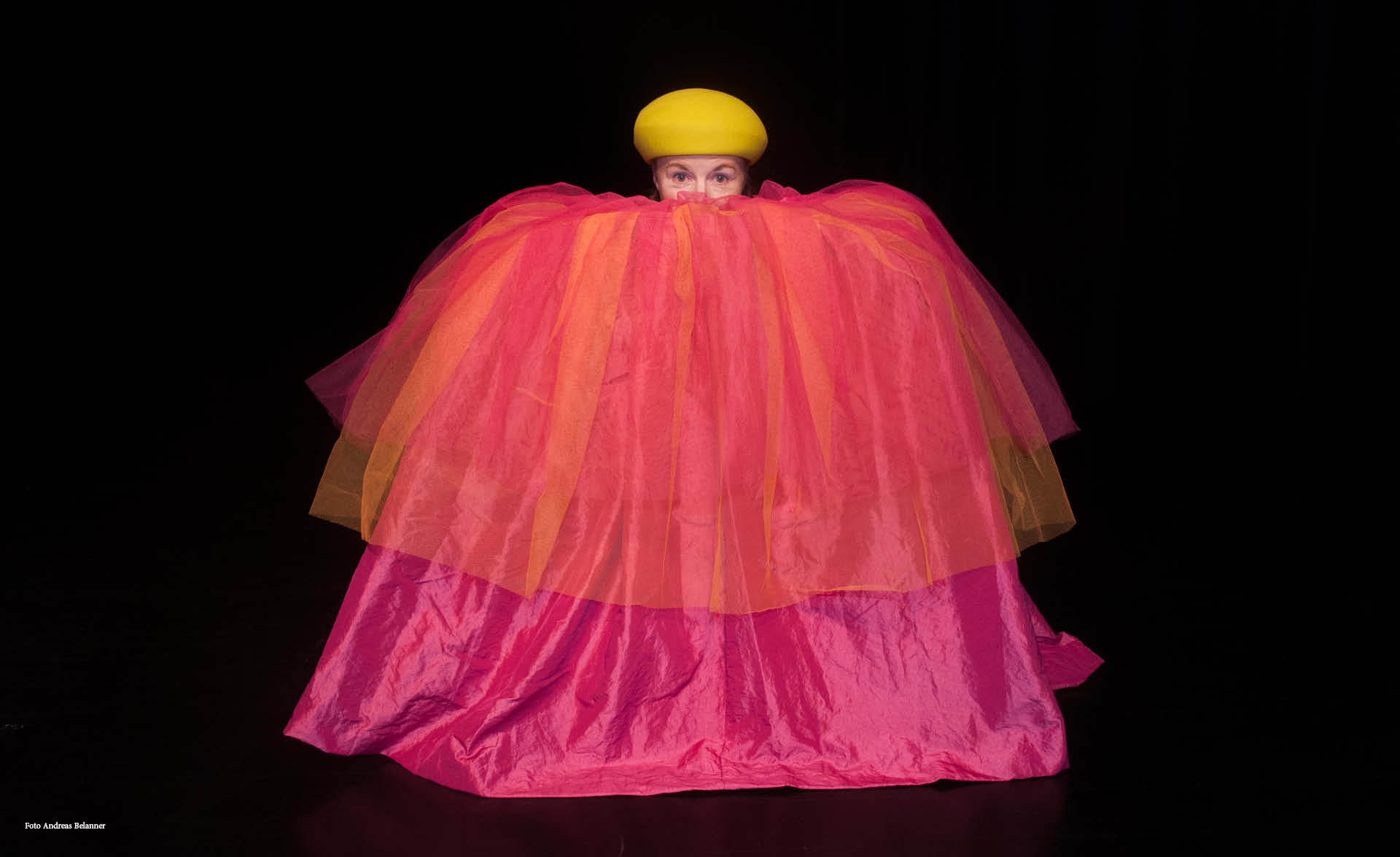 Ett ansikte med gul mössa tittar fram ur en stor rosa klänning.