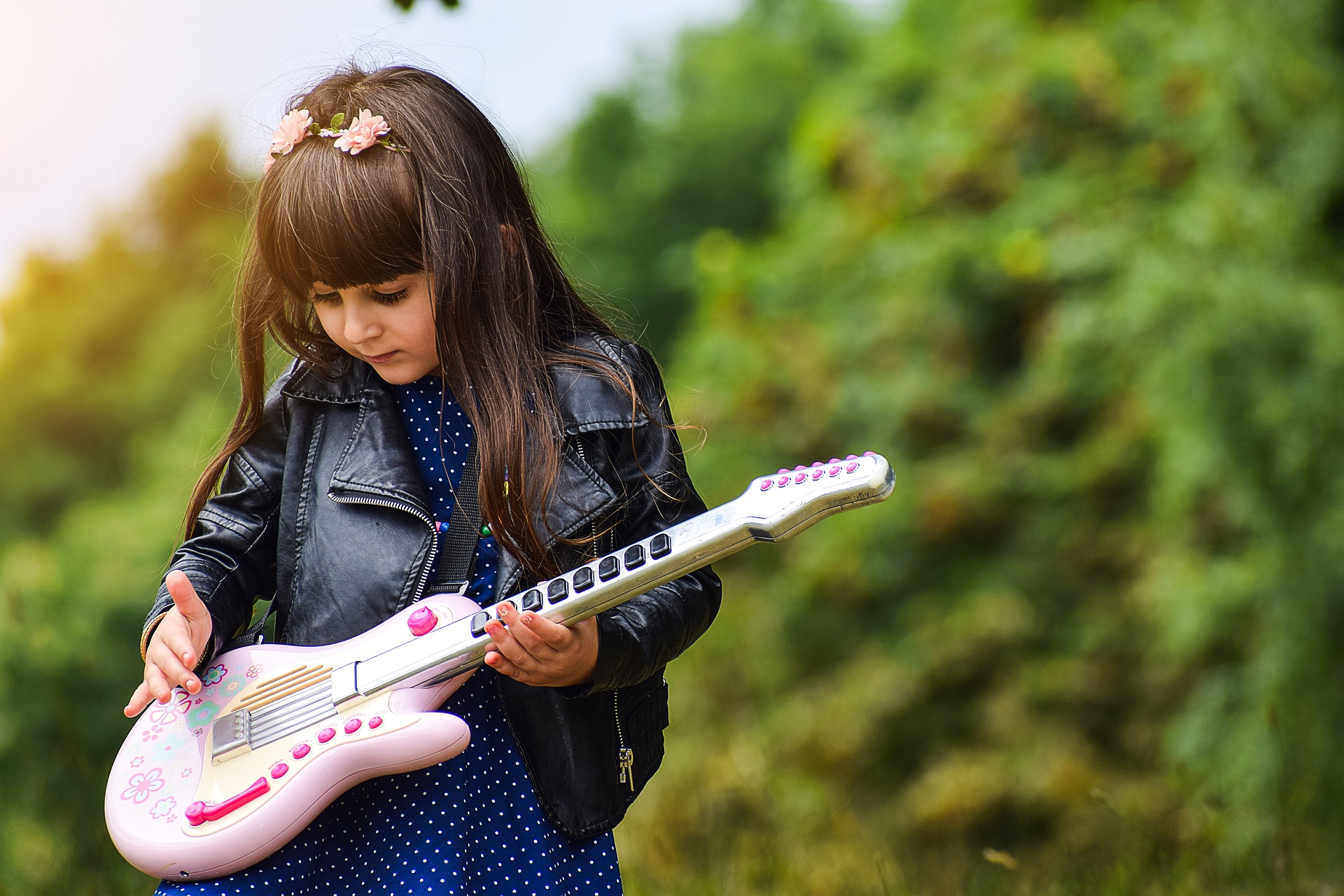En ung tjej spelar gitarr mot en grönskande bakgrund