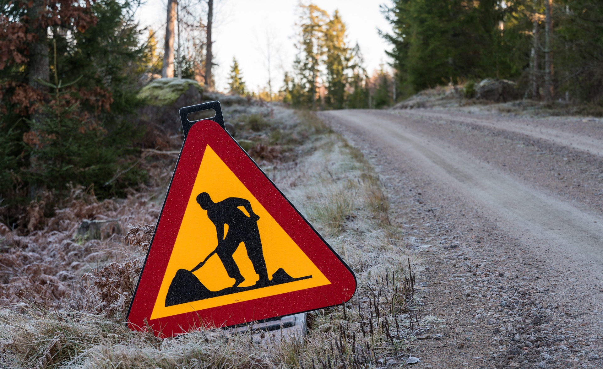 Traffic sign with warning for road work by a gravel road side in a forest